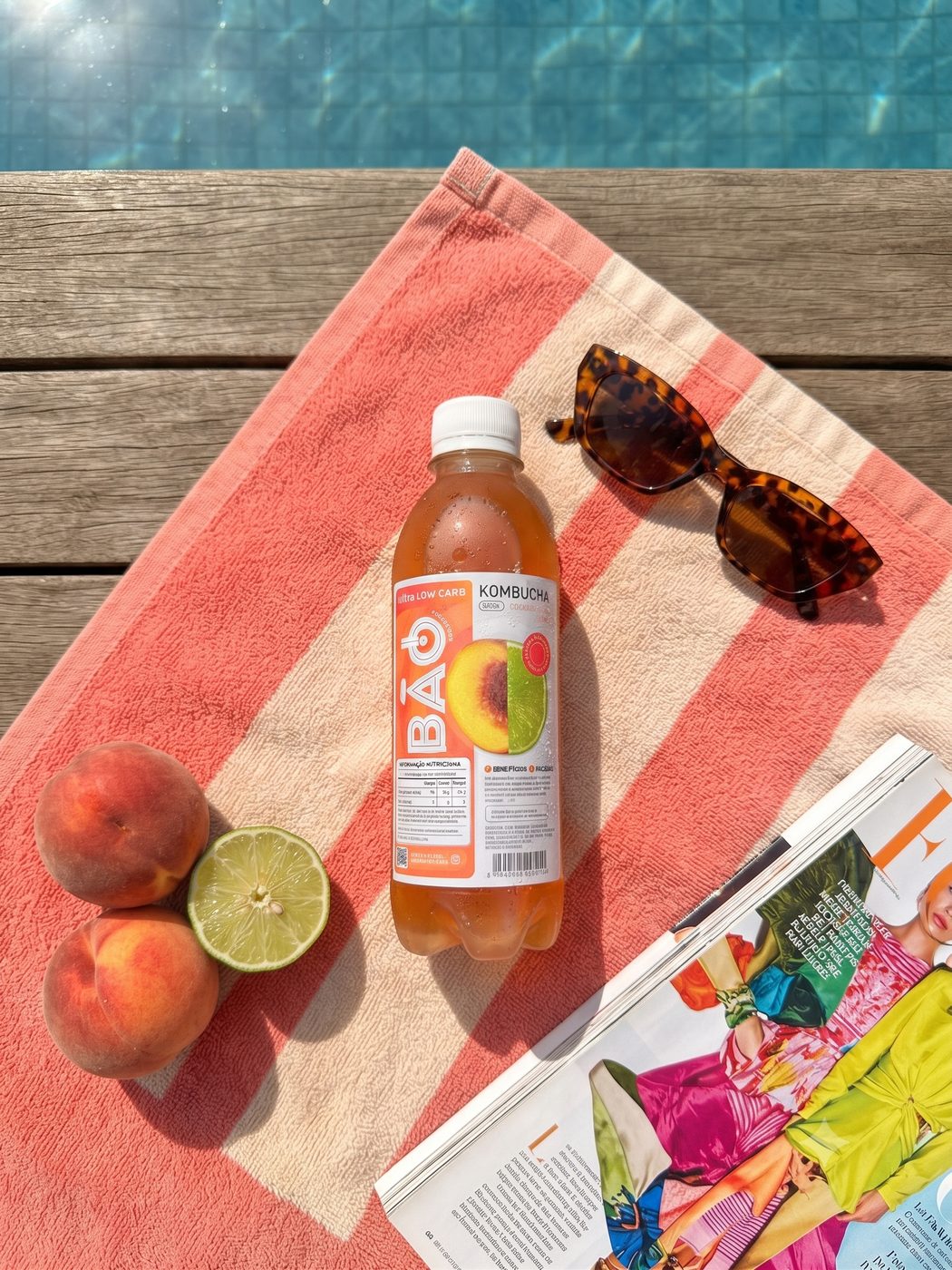 Kombucha Bão Pêssego & Limão na beira da piscina com óculos de sol e revista